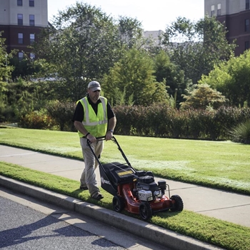 Landscape pro mowing grass with an Exmark Commercial 21 X-Series mower along a curb.