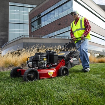 Pro mowing the grass with a Commercial 21 X-Series mower in front of a commercial building.