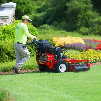 Professional landscaper using a Turf Trace S-Series mower to cut the grass next to a flower bed.